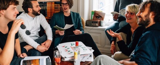 Teamfoto von Hermes Baby: 6 Redaktionsmitglieder am Tisch mit einem Stapel Pizzakartons und einer Vodkaflasche