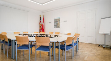 Raum mit Sesseln um runden Tisch, Amerikaflagge, Österreichflagge in der Ecke