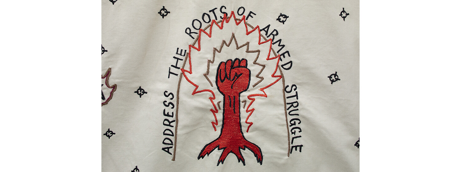 gesticktes Motiv mit einer roten Faust und dem Schriftzug ADDRESS THE ROOTS OF ARMED STRUGGLE