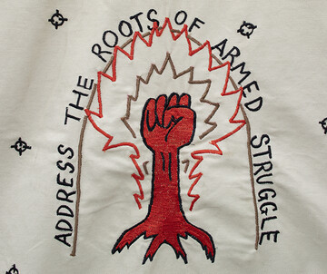 gesticktes Motiv mit einer roten Faust und dem Schriftzug ADDRESS THE ROOTS OF ARMED STRUGGLE