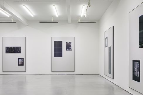 Gallery room with white walls and several framed photographs or prints of various sizes showing abstract or architectural motifs.