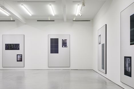 Gallery room with white walls and several framed photographs or prints of various sizes showing abstract or architectural motifs.