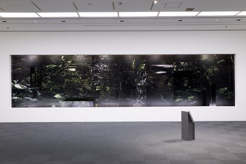 Large dark abstract artwork with indistinct shapes on a white museum wall with a small gray pedestal in front.
