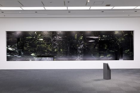 Large dark abstract artwork with indistinct shapes on a white museum wall with a small gray pedestal in front.