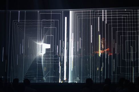 Several people stand behind a transparent surface with a complex geometric line pattern of rectangles and vertical lines.