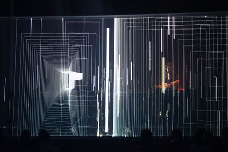 Several people stand behind a transparent surface with a complex geometric line pattern of rectangles and vertical lines.