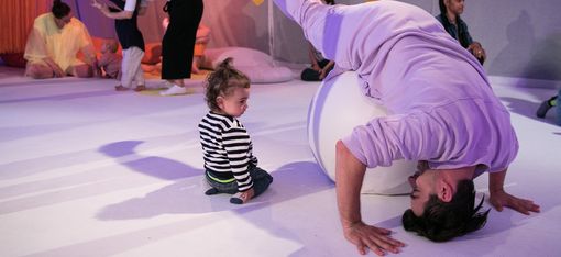 Das Foto zeigt Künstler:innen, die ganz junge Kinder dazu einladen, die Objekte auf der Bühne zu berühren und mit ihnen zu spielen.