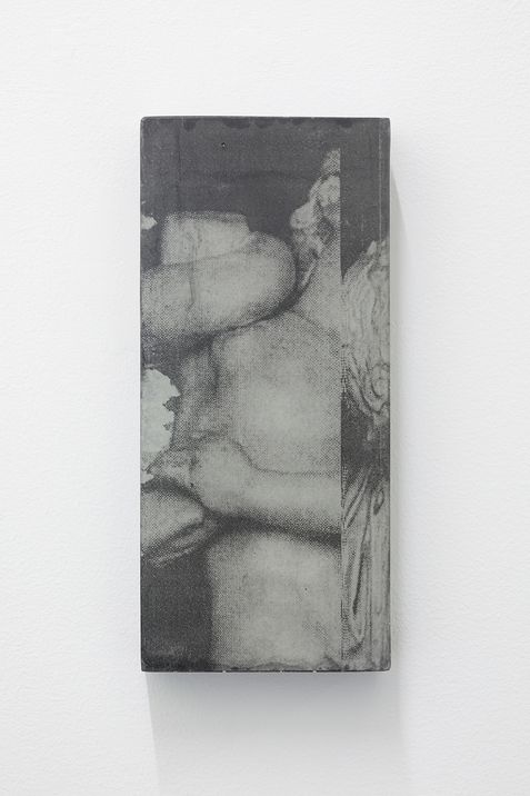 Black-and-white photograph of a bare torso and a face partially covered by a hand on a rectangular object.