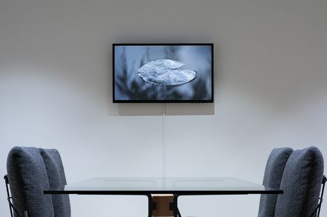 Two upholstered chairs at a glass table in front of a wall-mounted screen displaying a close-up of a leaf.