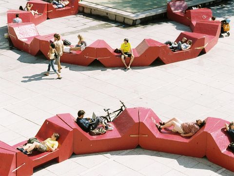 Menschen entspannen auf roten MQ Sitzmöbeln rund um das Wasserbecken im MuseumsQuartier Wien