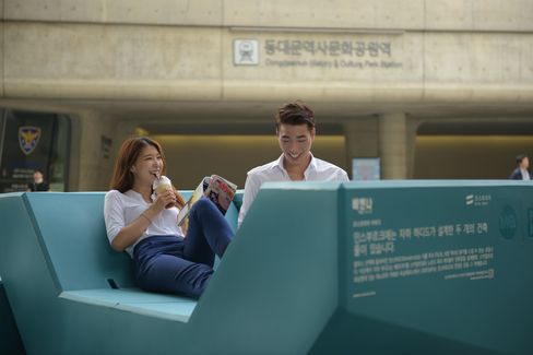 Zwei Personen sitzen entspannt auf einem Enzi-Sitzmöbel und lesen in einem belebten Stadtraum.