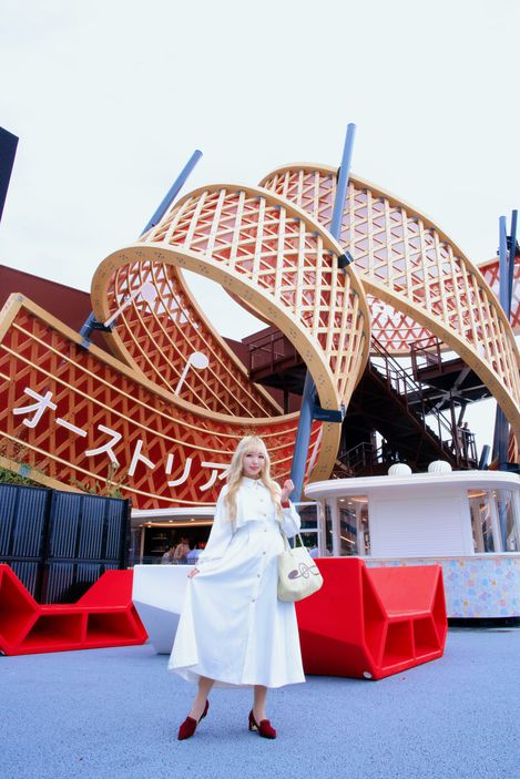 Enzi Sitzmöbel vor dem Österreich-Pavillon auf der Expo in Japan, mit einer Besucherin in weißem Kleid im Vordergrund und der markanten, geschwungenen Holzstruktur des Pavillons im Hintergrund