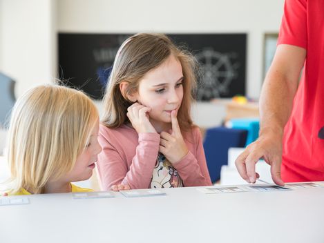 Zwei Kinder schauen auf eine Karte. Eines der beiden Kinder hat den Finger auf dem Mund