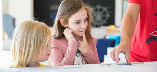 Zwei Kinder schauen auf eine Karte. Eines der beiden Kinder hat den Finger auf dem Mund