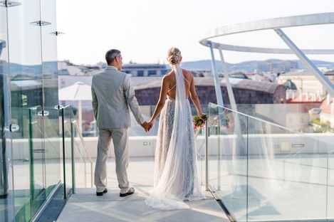 Wedding ceremony at MQ Libelle, MuseumsQuartier Vienna. A couple in wedding attire stands on the roof terrace and looks out over the rooftops of Vienna.