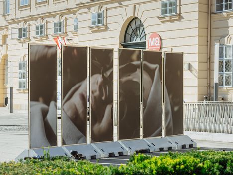 Four large photo panels with a portrait of a reclining person in front of  the MQ bulding