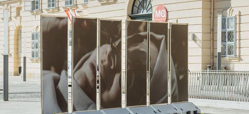 Four large photo panels with a portrait of a reclining person in front of  the MQ bulding