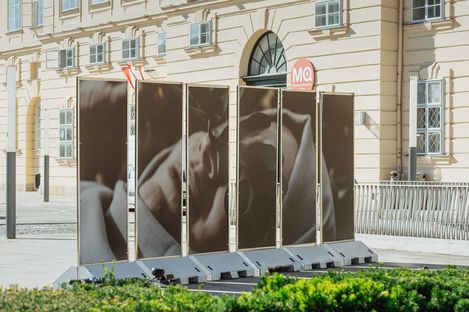Four large photo panels with a portrait of a reclining person in front of  the MQ bulding