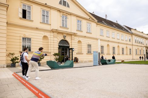 Two men playing boule in a sandy courtyard. One throws a metal ball towards a wooden target ball. They appear relaxed and focused.