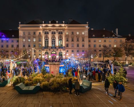Beleuchtetes historisches Gebäude bei Nacht mit großem Menschenauflauf und festlicher Dekoration im Vordergrund