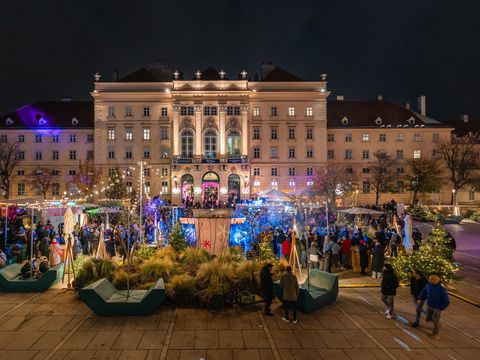 Beleuchtetes historisches Gebäude bei Nacht mit großem Menschenauflauf und festlicher Dekoration im Vordergrund