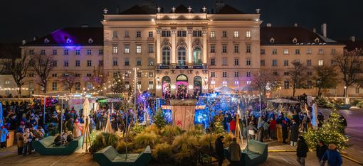 Beleuchtetes historisches Gebäude bei Nacht mit großem Menschenauflauf und festlicher Dekoration im Vordergrund