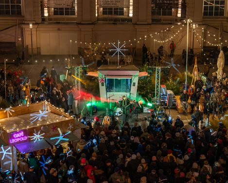 Menschenmenge bei einem nächtlichen Open-Air-Konzert mit beleuchtetem Bühnenaufbau und Dekorationen in einem Innenhof