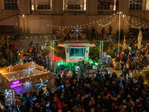 Menschenmenge bei einem nächtlichen Open-Air-Konzert mit beleuchtetem Bühnenaufbau und Dekorationen in einem Innenhof