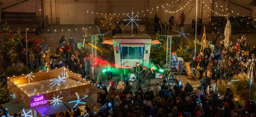 Menschenmenge bei einem nächtlichen Open-Air-Konzert mit beleuchtetem Bühnenaufbau und Dekorationen in einem Innenhof