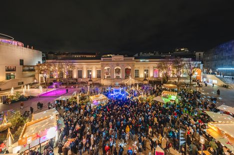 Große Menschenmenge auf einem beleuchteten Weihnachtsmarkt vor einem historischen Gebäude bei Nacht