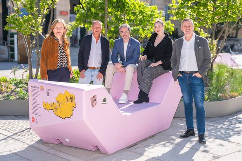 Group of five people sitting and standing around a pink Enzi in the MuseumsQuartier courtyard.