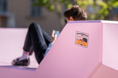 Detail eines rosa Enzis mit MuseumsQuartier Wien Sticker; eine Person sitzt unscharf im Hintergrund.