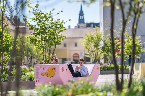 Person sitzt entspannt auf einem rosa Enzi im begrünten Hof des MuseumsQuartier und blickt auf ihr Smartphone.