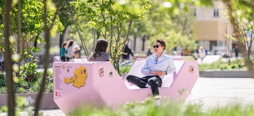 Zwei Personen sitzen sich auf einem rosa Enzi gegenüber und unterhalten sich im MuseumsQuartier Hof.