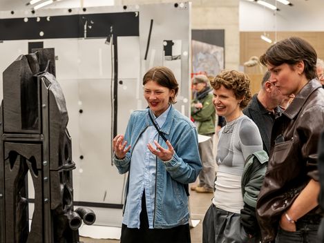 Drei Personen betrachten eine Skulptur aus Keramik und Metall in einem Ausstellungsraum und unterhalten sich angeregt.