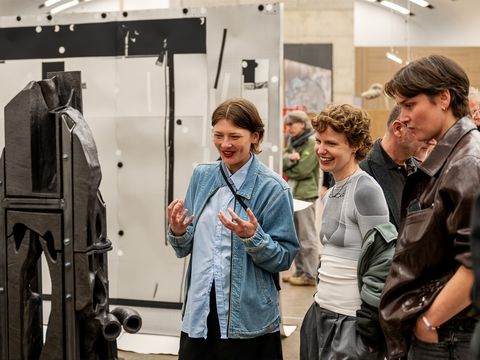 Drei Personen betrachten eine Skulptur aus Keramik und Metall in einem Ausstellungsraum und unterhalten sich angeregt.