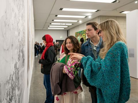 Three people are looking at a painting.
