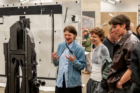 Drei Personen betrachten eine Skulptur aus Keramik und Metall in einem Ausstellungsraum und unterhalten sich angeregt.