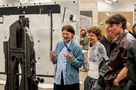 Drei Personen betrachten eine Skulptur aus Keramik und Metall in einem Ausstellungsraum und unterhalten sich angeregt.