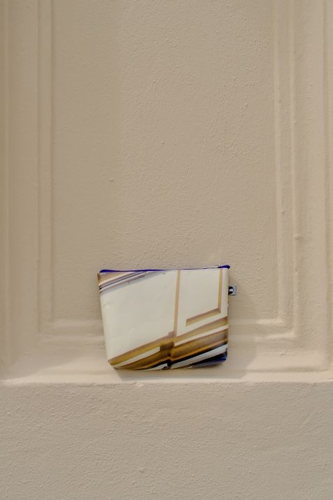 Kleine Tasche mit abstraktem Muster lehnt an einer hellen Wand mit vertieften Linien