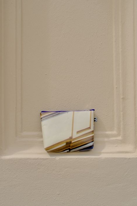 Kleine Tasche mit abstraktem Muster lehnt an einer hellen Wand mit vertieften Linien