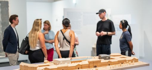 Gruppe von sechs Personen steht vor einem Architekturmodell in einem Ausstellungsraum
