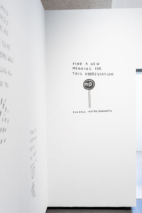 Weiße Wand mit schwarzer Schrift und einer Zeichnung eines runden Schilds mit den Buchstaben 'mq' und dem Text 'FIND A NEW MEANING FOR THIS ABBREVIATION EXAMPLE: METRO QUADRATO'