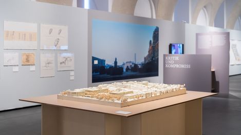 Model of an urban landscape on a table in an exhibition room with photographs and text panels on the walls.