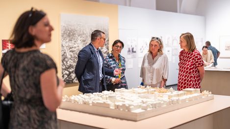Vier Personen stehen um ein Architekturmodell auf einem Tisch in einem Ausstellungsraum und unterhalten sich.