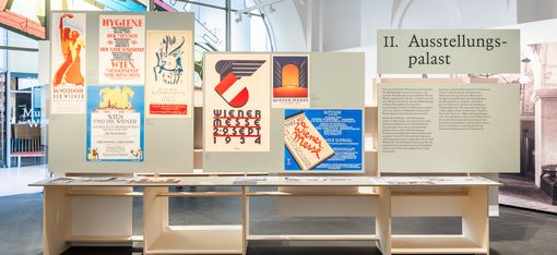 Exhibition space with several historical posters on display panels and a sign reading 'II. Ausstellungspalast'
