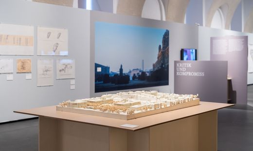 Model of an urban landscape on a table in an exhibition room with photographs and text panels on the walls.