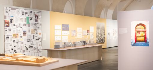 Exhibition room with models, wall panels, and photographs in a vaulted ceiling space
