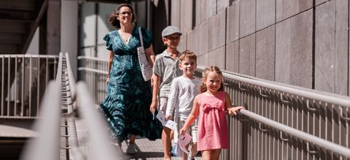 Eine Familie geht mit den Unterlagen des MQ-Rätselparcours über eine Rampe im MuseumsQuartier und erkundet das Gelände.