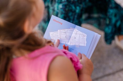 Ein Mädchen hält den Plan des MQ-Rätselparcours in den Händen und betrachtet aufmerksam den eingezeichneten Weg durch das MuseumsQuartier.